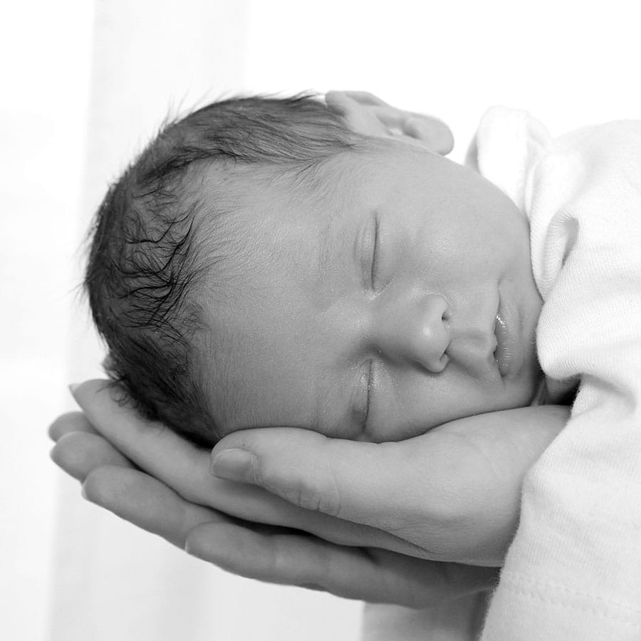 Ein Babykopf in den Händen eines Erwachsenen